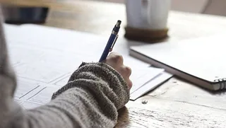 Hand schreibt mit Stift auf Papier.