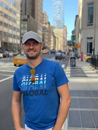 English: Man in a t-shirt and cap on a city street. 