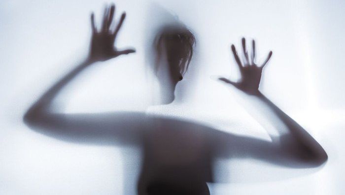 Silhouette einer Person mit erhobenen Händen hinter Stoff.