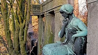 Statue einer sitzenden, nachdenklichen Frau auf einem steinernen Bauwerk.