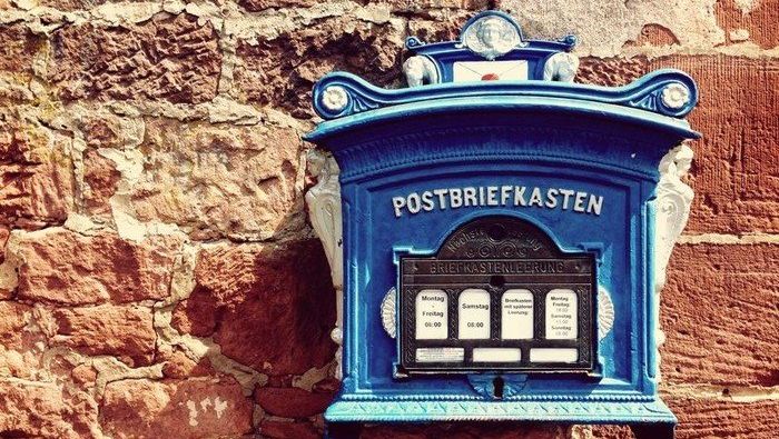 Blaue, historische Postbriefkasten an einer steinernen Mauer.