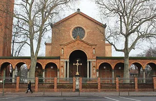Backsteinkirchenfassade mit Torbögen und einem Kreuz.