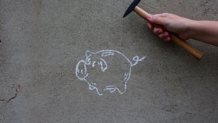 Hand mit Hammer neben Kreide-Sparschwein.