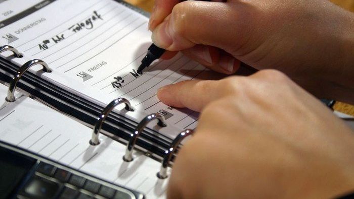 Hände schreiben in einen offenen Ringbuchkalender.