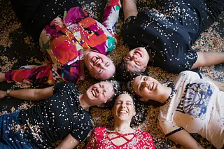 Sechs Frauen sitzen auf einer roten Bank vor einer beschriebenen Tafel.