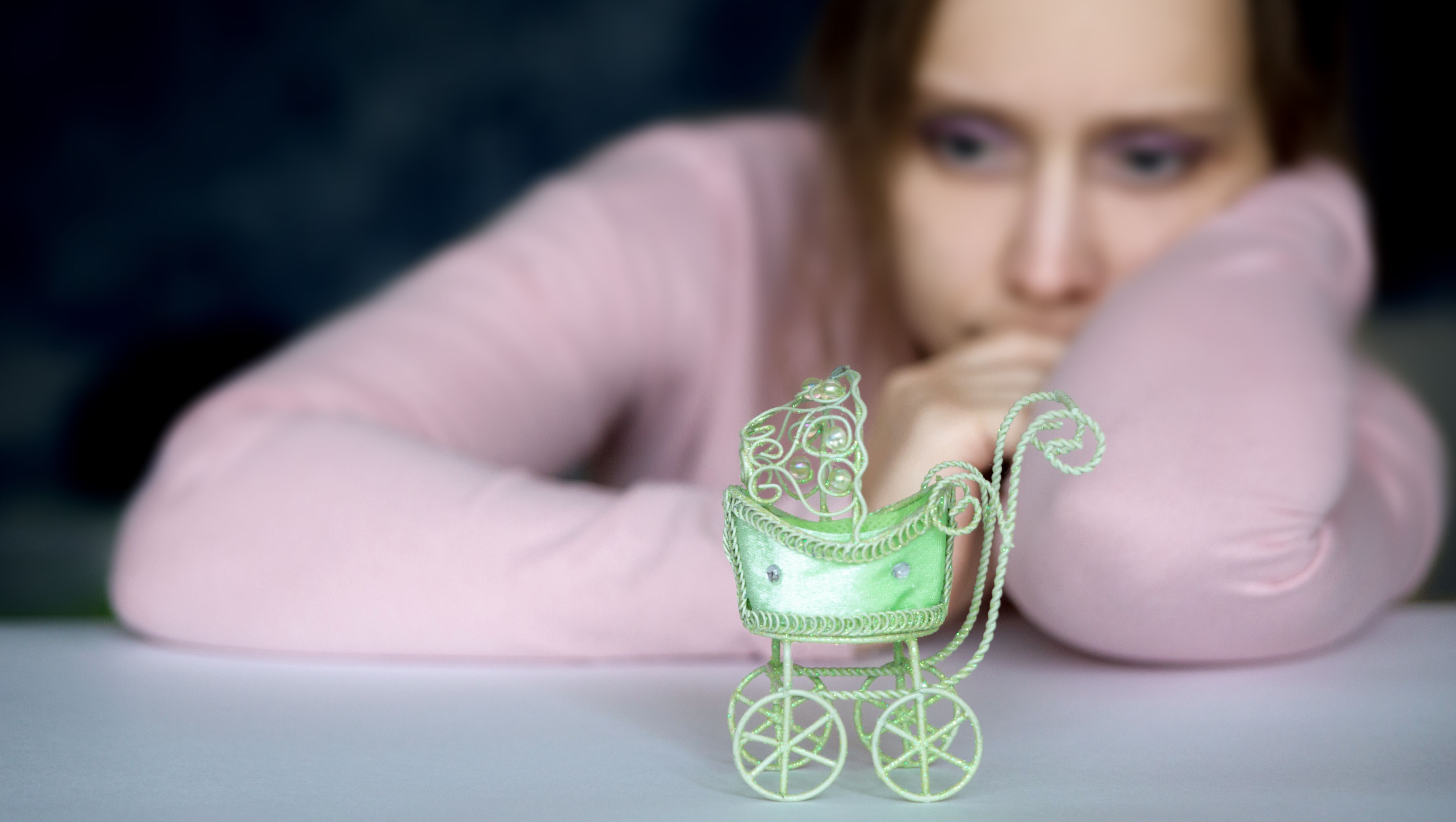 Frau blickt auf einen Miniatur-Kinderwagen.