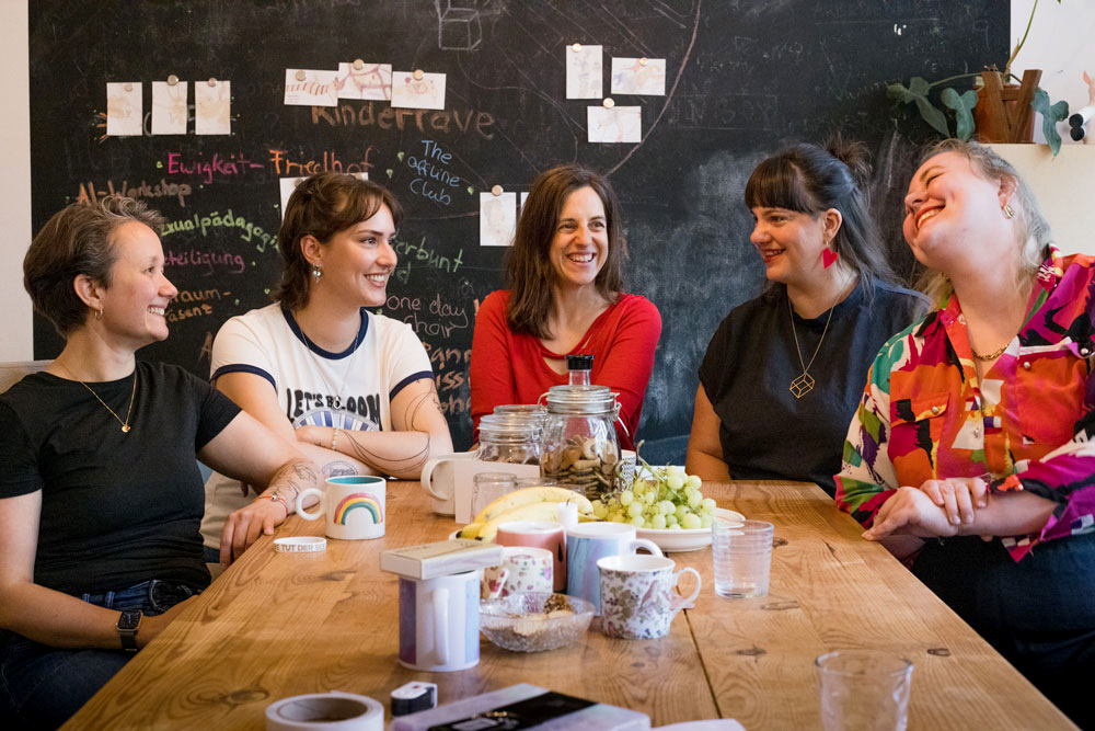 Gruppe von fünf Frauen sitzt vor einer dunklen Wand.
