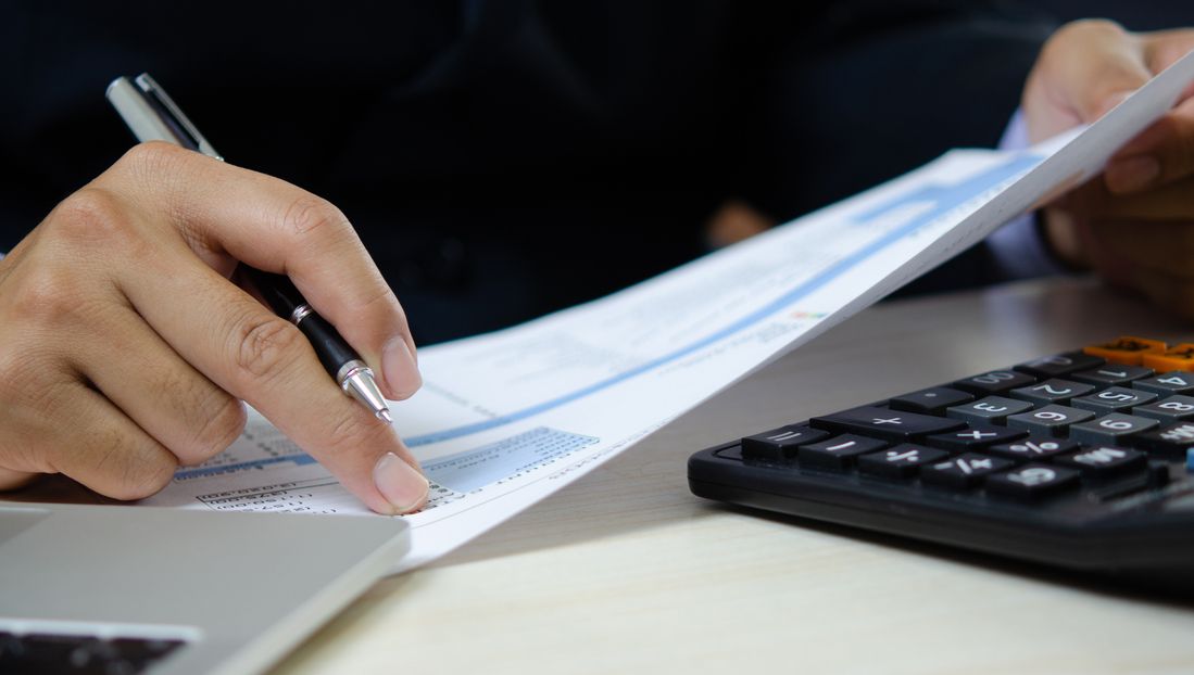 Person prüft Dokumente mit einem Taschenrechner.