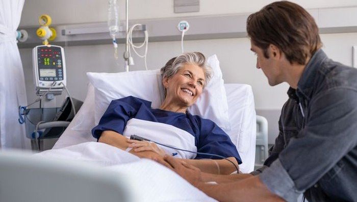 Mann besucht lächelnden Patienten im Krankenhaus.